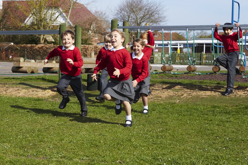 Niños con uniforme escolar corriendo en un jardín